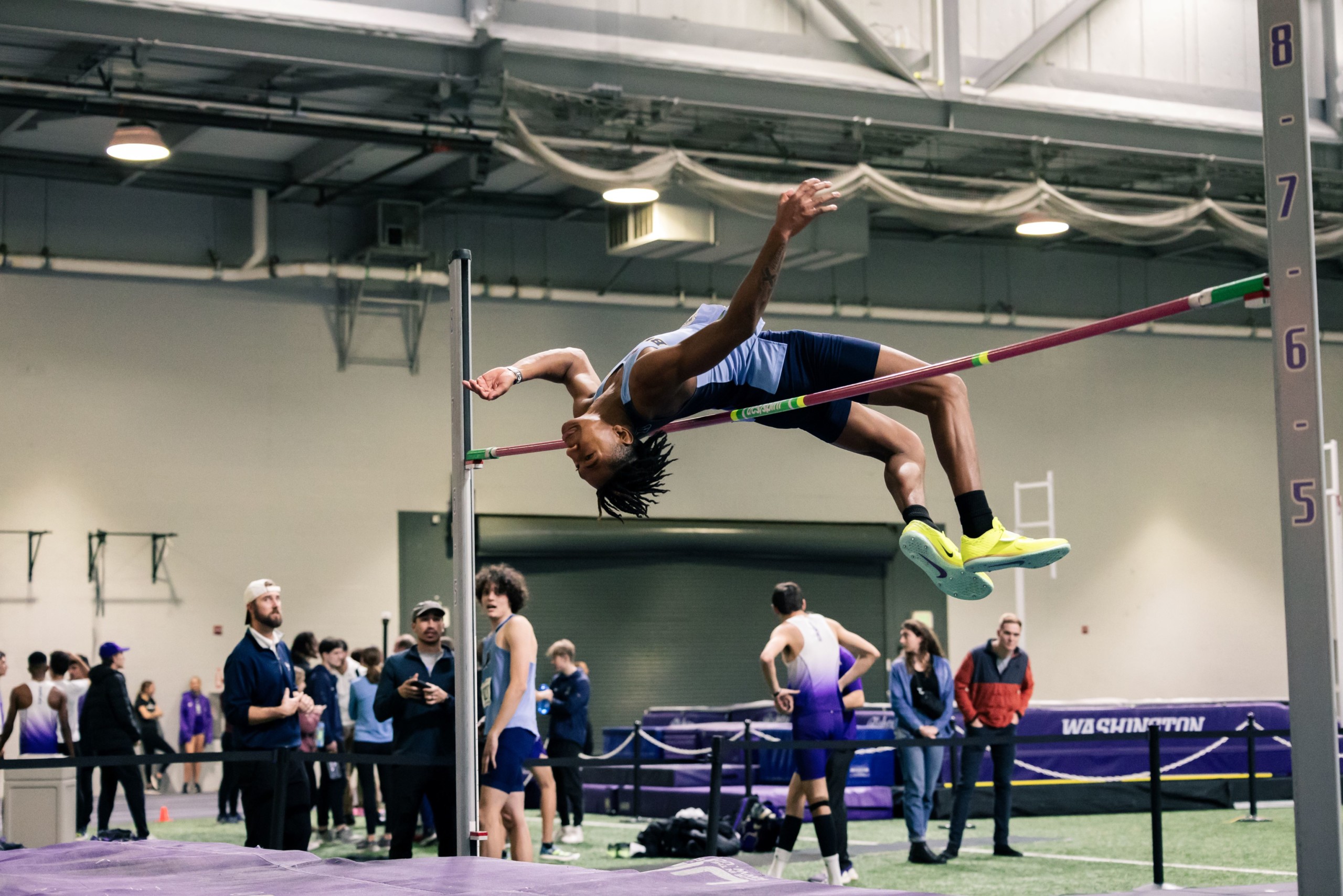male athlete in midair on the high jump at an indoor track and field competition