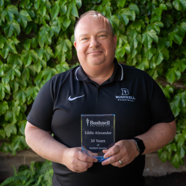 Employee recognized for 10 years of faithful service while holding a commemorative award outdoors on campus