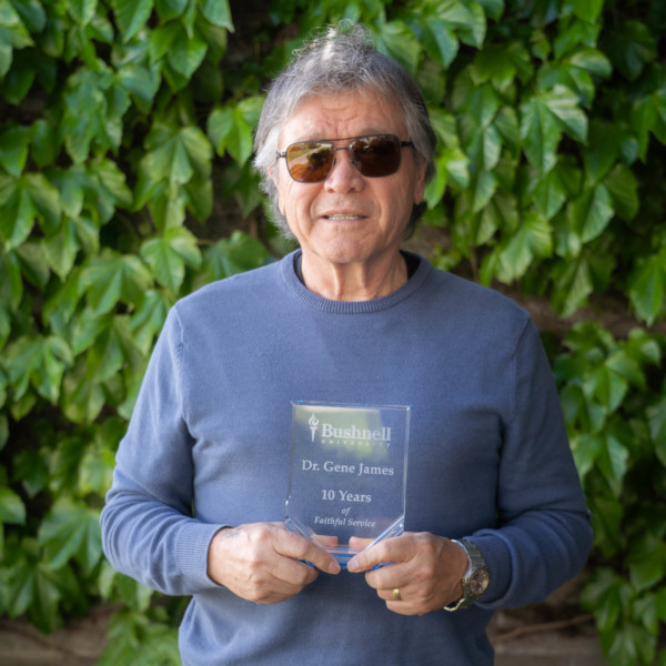 Employee recognized for 10 years of faithful service while holding a commemorative award outdoors on campus