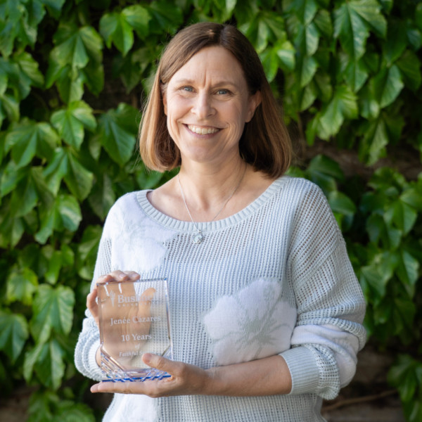 Employee recognized for 10 years of faithful service while holding a commemorative award outdoors on campus