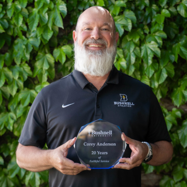 Employee recognized for 20 years of faithful service while holding a commemorative award outdoors on campus