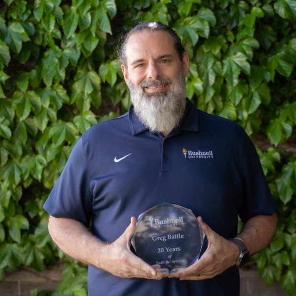 Employee recognized for 20 years of faithful service while holding a commemorative award outdoors on campus