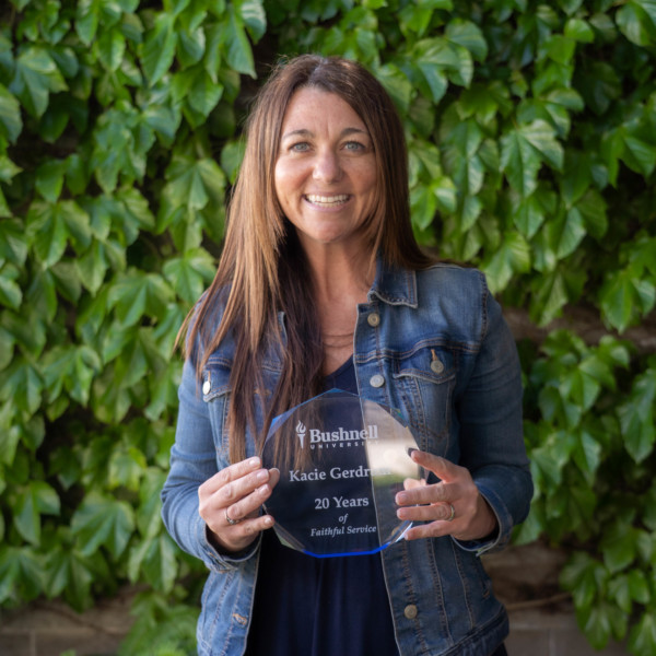 Employee recognized for 20 years of faithful service while holding a commemorative award outdoors on campus
