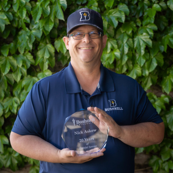 Employee recognized for 20 years of faithful service while holding a commemorative award outdoors on campus