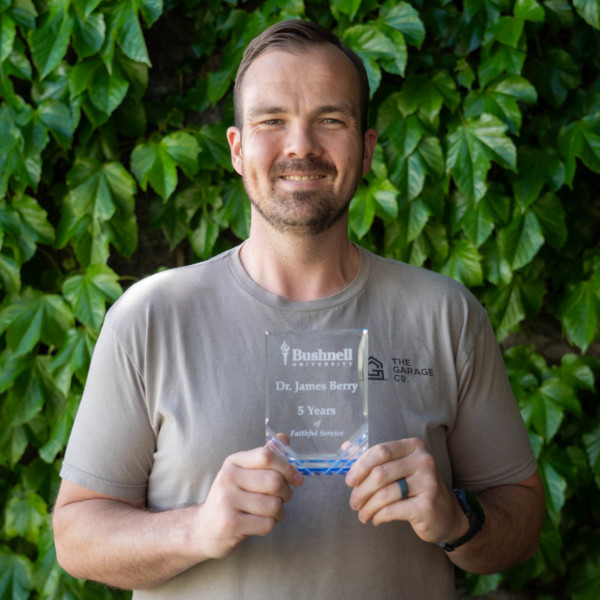Employee recognized for 5 years of faithful service while holding a commemorative award outdoors on campus