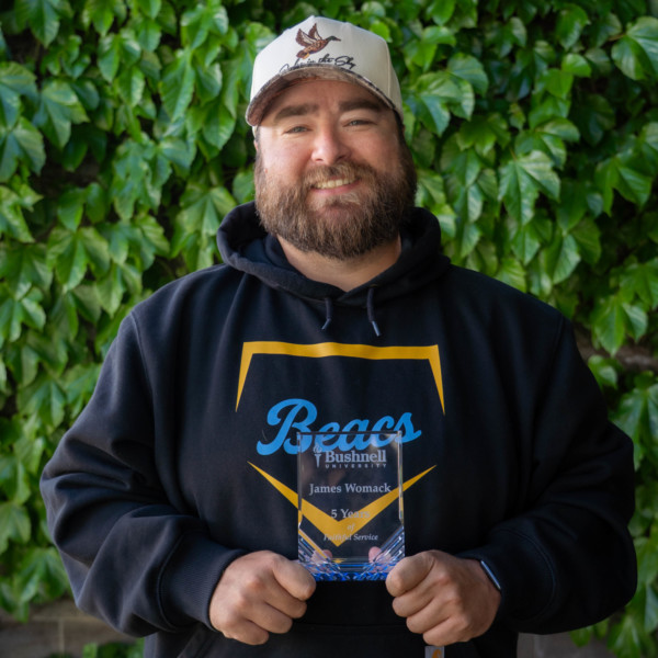 Employee recognized for 5 years of faithful service while holding a commemorative award outdoors on campus