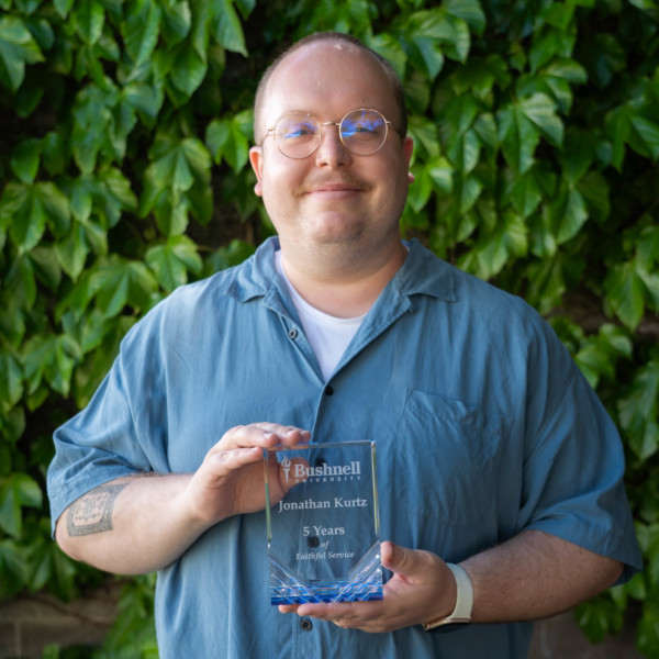 Employee recognized for 5 years of faithful service while holding a commemorative award outdoors on campus