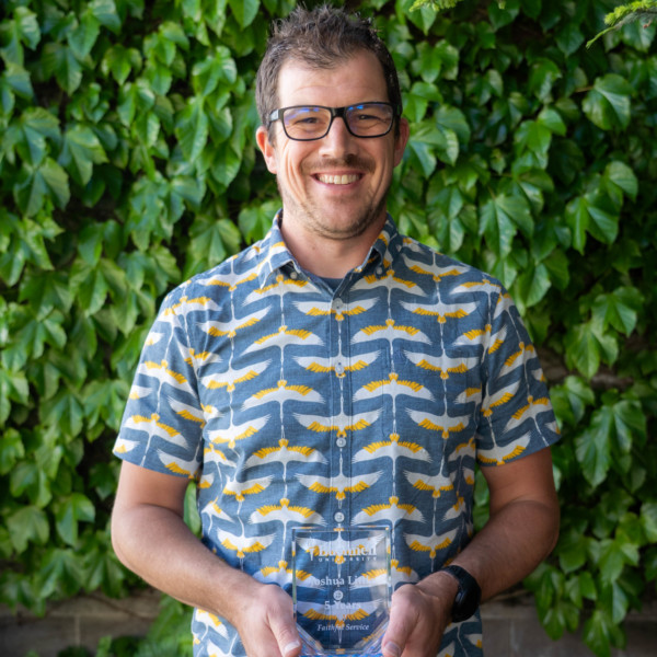 Employee recognized for 5 years of faithful service while holding a commemorative award outdoors on campus