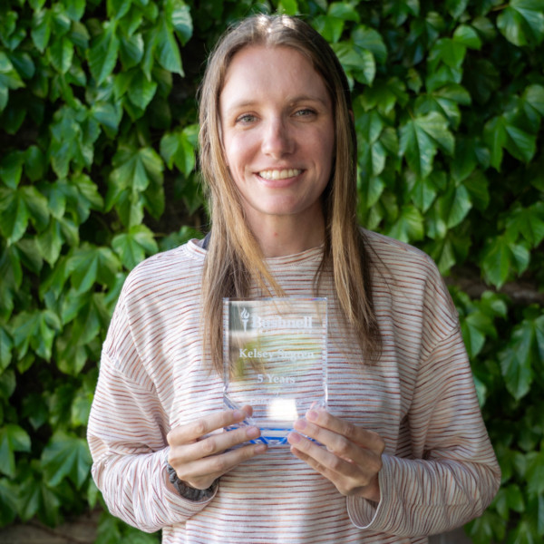 Employee recognized for 5 years of faithful service while holding a commemorative award outdoors on campus