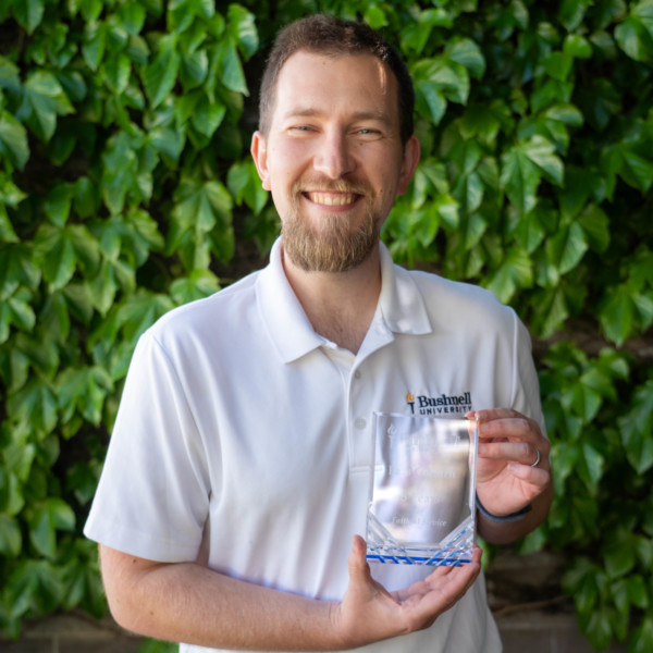 Employee recognized for 5 years of faithful service while holding a commemorative award outdoors on campus