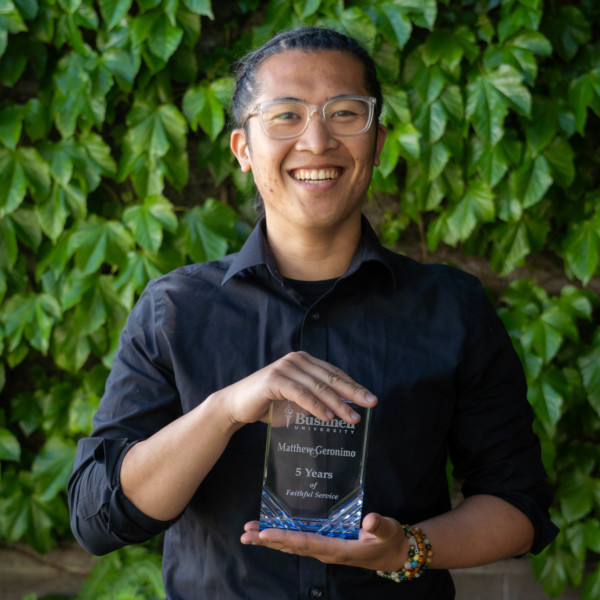 Employee recognized for 5 years of faithful service while holding a commemorative award outdoors on campus