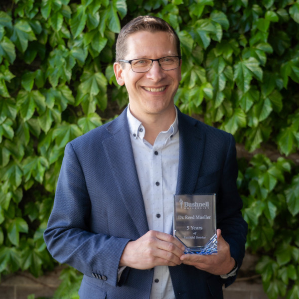 Employee recognized for 5 years of faithful service while holding a commemorative award outdoors on campus